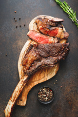 Top view of grilled dry-aged marble beef steak Tomahawk on black wooden board with spices. Flat...