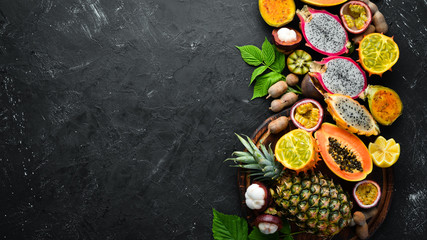 Obraz na płótnie Canvas Tropical fruits: papaya, mangosteen, cactus fruit, pytahaya, pineapple on a black background. Top view. Free space for text.