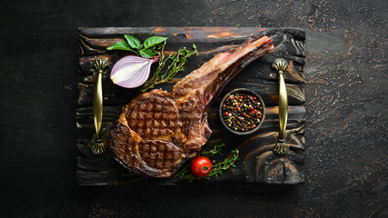 Grilled steak on the bone, herbs and spices on a wooden background. Barbecue. Top view. Free space...