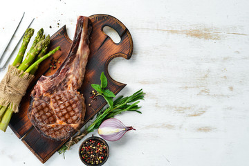 Grilled steak on a bone on a white wooden background. Barbecue. Top view. Free space for text.
