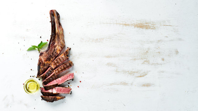 Grilled steak on the bone sliced, herbs and spices on Wooden background. Barbecue. Top view. Free space for text.
