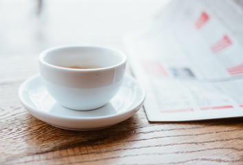 Still life image of cup of black coffee with fresh sport newspaper on the wooden table next to big coffee shop window.