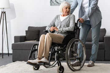 Fototapeta na wymiar cropped view of man carrying senior mother on wheelchair