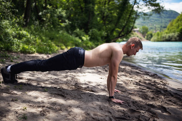 Active muscular man doing push up on sand