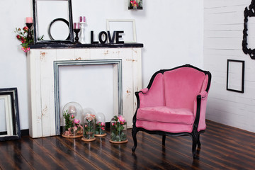 Fototapeta na wymiar Vintage velor armchair, in a bright room and an artificial fireplace. Interior attic with wooden white walls. Picture frames on the wall. The space where you can put a person. Gothic style room. 