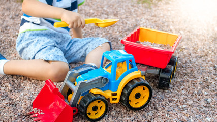 Portrait of adorable 3 years old toddler boy playing with toy truck with trailer on the playground...