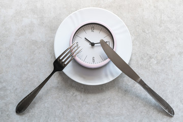 Pink alarm clock on a white plate with metal utensils. Dieting/ eating concept.