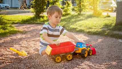 Closeup portrait of happy smiling 3 years old child boy digging sand on the playground with toy...