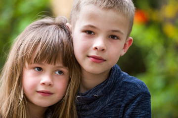 Two cute fair-haired children siblings, young boy brother and sister girl outdoors on bright sunny green bokeh background. Family relation, friendship and love concept.
