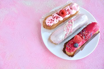 Beautiful traditional French eclairs cake with creative pink decor and fresh berries on pink textured table. Selective focus. Tasty dessert profiteroles with pink and red icing and sugar decor element
