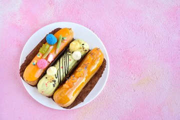French delicious fresh eclairs with yellow icing and sugar colorful raspberries on pink textured...