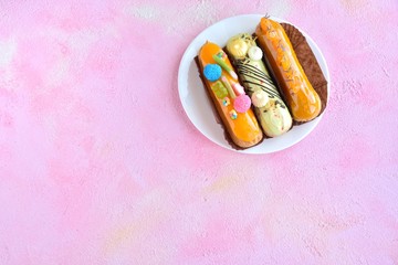 French delicious fresh eclairs with yellow icing and sugar colorful raspberries on pink textured background. Sweet tasty profiteroles on white plate with creative colorful decor. Traditional eclair