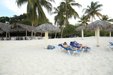 Summer holidays and vacations-young man and a young woman are resting together on the beach with white sand on a blue lounge chair against the backdrop of coconut palm trees and natural umbrellas 