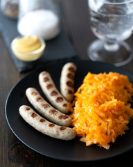 Braised cabbage and grilled bratwurst served with mustard and a glass of water. Dark background, high resolution