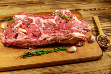 Raw fresh beef rib eye steak on bone with spices, garlic and rosemary on wooden table