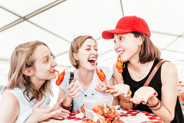 Group of happy young multiracial girl friends eating sea food crawfish at a outdoor restaurant