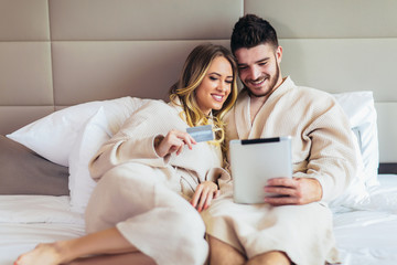 Young happy couple shopping online in luxury hotel room.