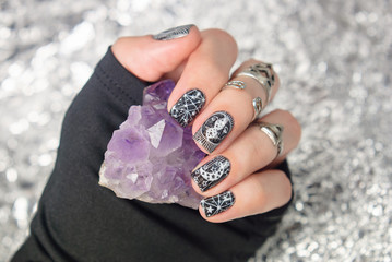 Black gothic manicure with mystic nail art. Amethyst in the hand on the silver sparkle background.