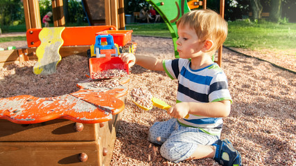Portrait of little 3 years old toddler boy sitting on the playground and digging sand with toy plastic spade © Kyrylo Ryzhov