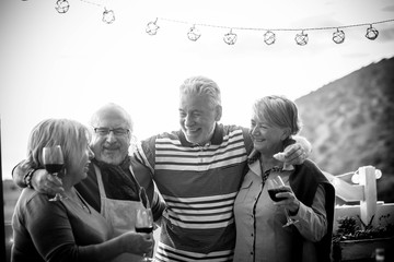Black and white group of senior aged friends people celebrating together outdoor with wine glasses...
