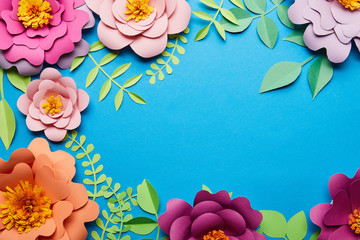 top view of multicolored bright paper cut flowers with green leaves on blue background with copy space