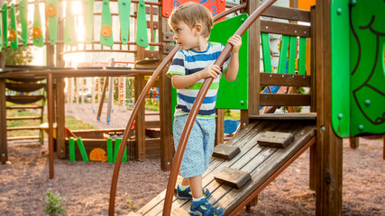 Portrait of active little boy crawling and climbing on wooden staircase on children playground at...