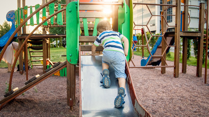 Image of happy smiling cheerful toddler boy riding and climbing on the big children playground at...