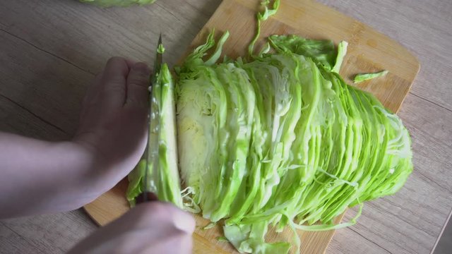 female hands cut green cabbage cabbage on a wooden surface of a kitchen table, top view