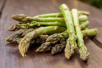 Cultivated, raw and fresh young green asparagus officinalis shoots, ready to cook. On a natural wooden surface. Healthy vegan cooking. Close up of shoots. 