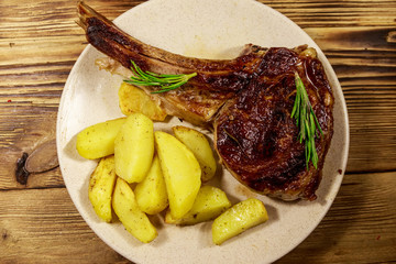 Roasted beef rib eye steak on bone with baked potatoes and herbs on wooden table