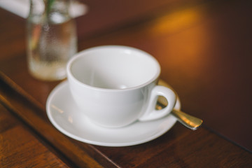 Close-up empty white cup with saucer and spoon on a table in a restaurant