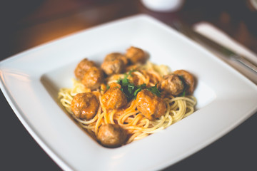 Close-up of spaghetti pasta with meatballs and tomato sauce in a white plate on the table in a restaurant