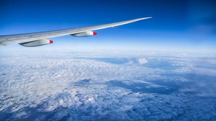 Close up of window with airplane wing. Beautiful cloudscape with clear blue sky.