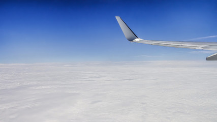 Fototapeta premium Close up of window with airplane wing. Beautiful cloudscape with clear blue sky.
