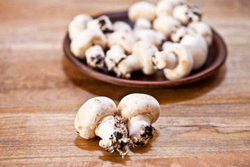 Fresh raw organic champignons on brown ceramic plate on wooden table.