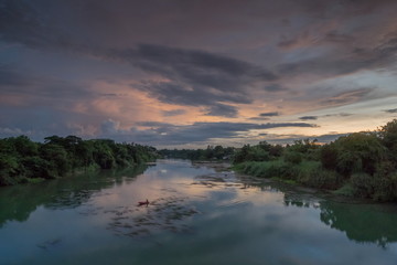 river view evening of a fishing boat floating in Mae Klong river around with forest on both bank with cloudy sky background, Ban Pong District, Ratchaburi, Thailand.