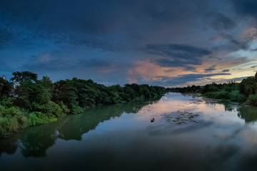 Fototapeta na wymiar river view evening of a fishing boat floating in Mae Klong river around with forest on both bank with cloudy sky background, Ban Pong District, Ratchaburi, Thailand.