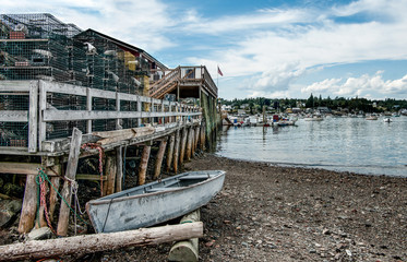 Fototapeta premium New England Fishing Port: A small boat waits beside a rough wooden pier piled high with lobster traps on a bay in southeast Maine.
