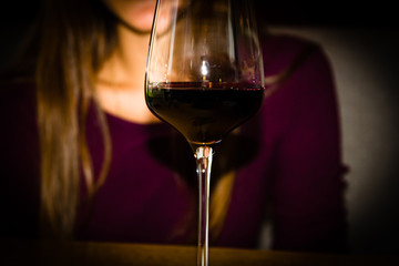 A young girl is sitting in a cafe. Before her is a glass of red wine. The general background of the picture is crimson.