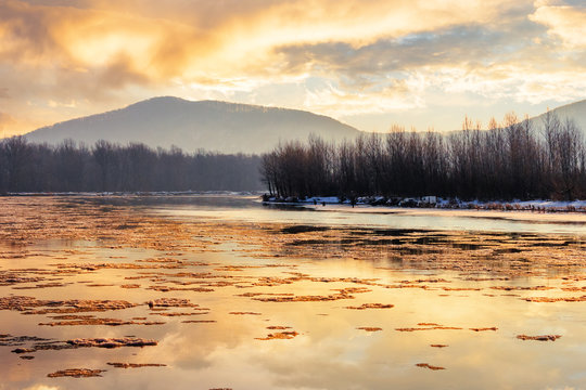 river in mountain at winter sunset. floating melting ice. cloudy sky reflecting in the water surface. wonderful nature scenery