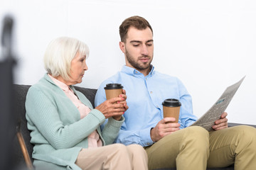 man and senior mother holding coffee and reading newspaper at home
