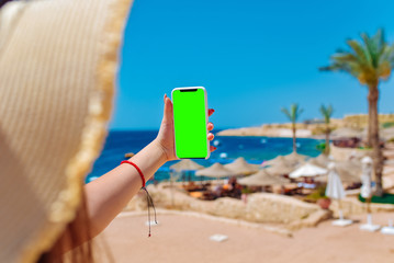 Young travelling woman blogger in hat taking photos of summer sunny sea with smartphone camera. Brunette girl making photography on summer vacation