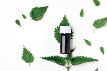 Bottle of essential oil with fresh nettle on white background. Natural herb essential from nature. Flat lay, top view, copy space