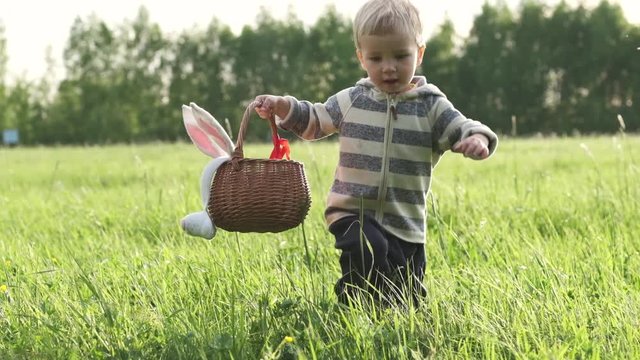Cute little kid with wicker basket searching for easter eggs on lawn in nature or park. Easter egg hunt. Slow motion.