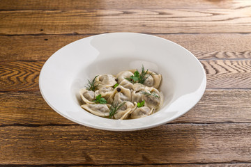 Russian meat dumplings pelmeni with black pepper on white plate isolated on wooden background