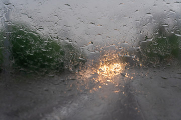 Drops from the rain on the windshield in the evening, in the background lights from the oncoming car