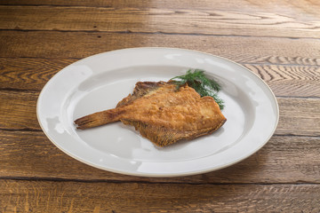 Fried fish flounder on white plate isolated on wooden background
