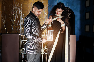 Happy diwali day! Lovely indian couple in love, wear at saree and elegant suit, posed on restaurant and hold lantern together.