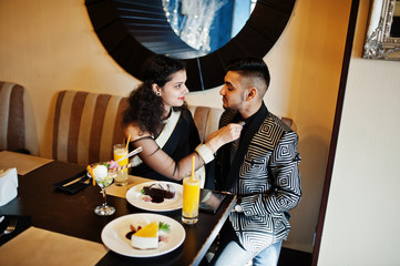 Lovely indian couple in love, wear at saree and elegant suit, posed on restaurant. Woman tied tie on her man.
