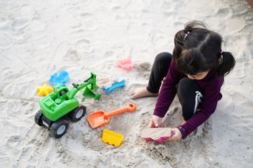 Happy Asian kid girl playing toy with and sand on the beach.